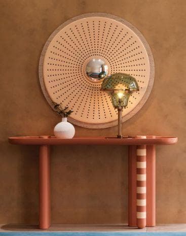 A terracotta console table beneath a round perforated wood mirror.