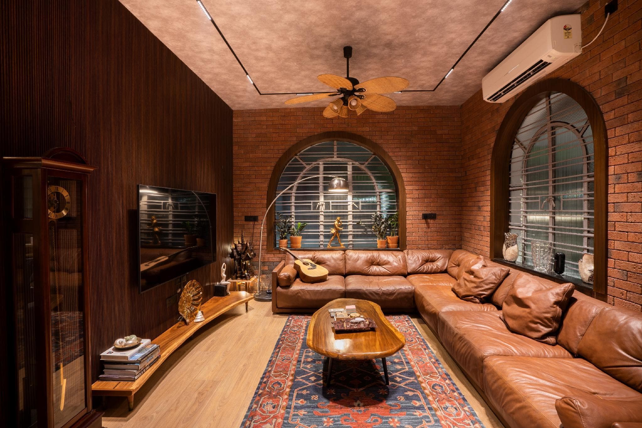 A living room with exposed brick walls, arched windows, and a tan leather sectional sofa around a live-edge wood coffee table.