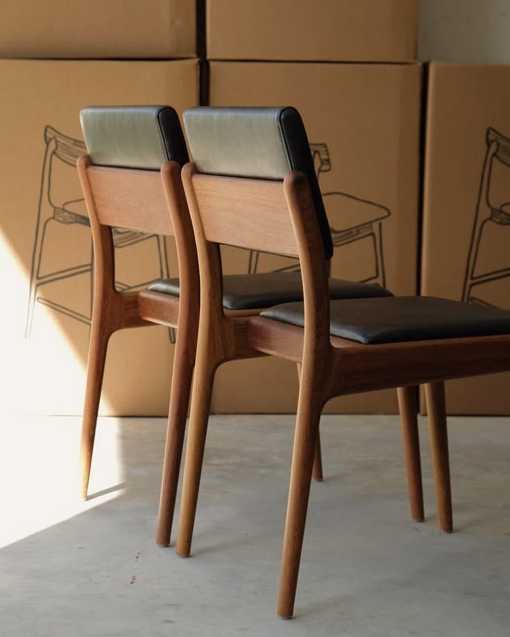 NOA premium wooden dining chair with sculpted wooden back, black upholstered seat and warm walnut frame shown in a dining setting.