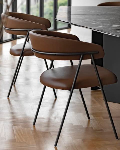 TALIA dining armchairs with curved brown upholstered seats and slim black metal frames in a contemporary dining setting.