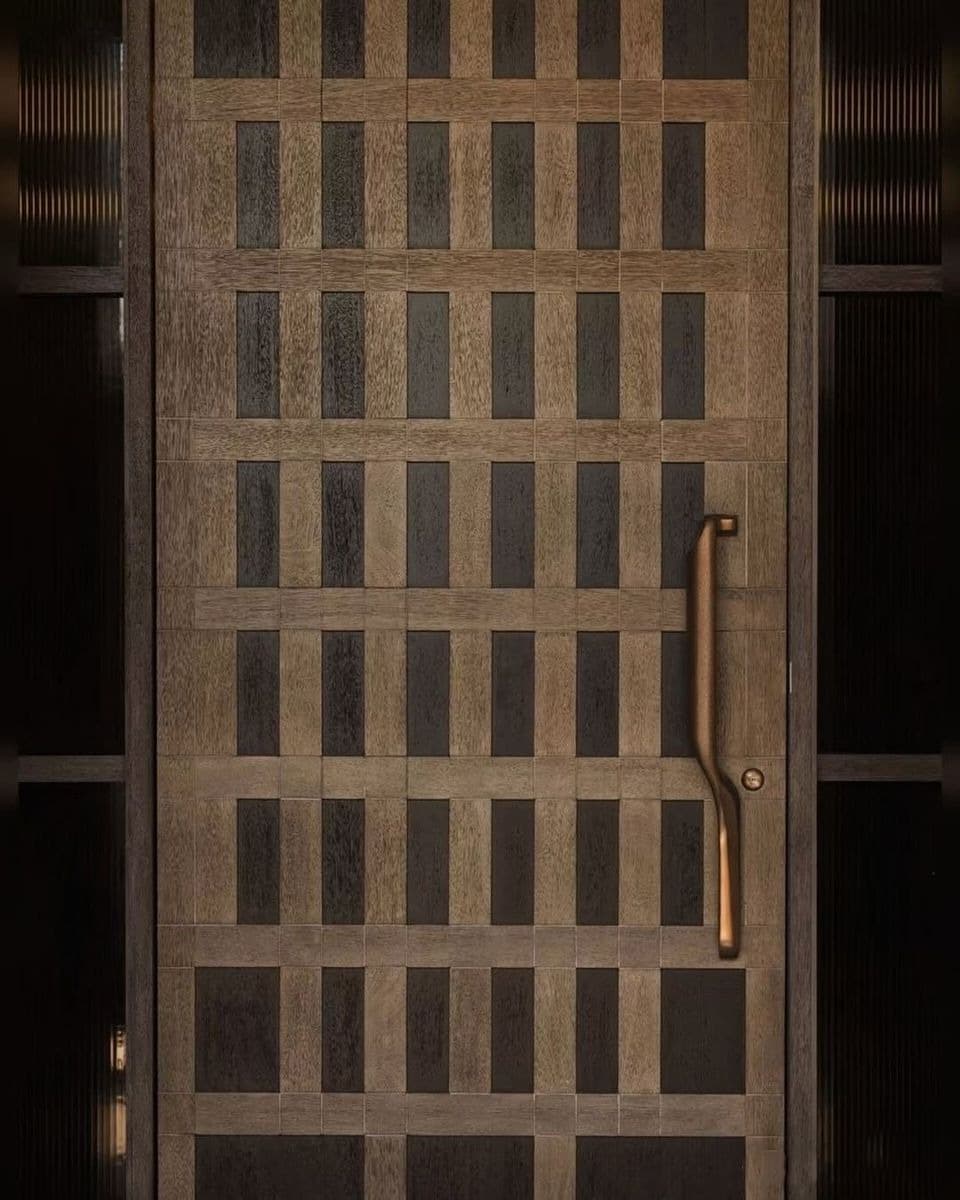 Lattice Grid Textured Main Door shown in a dark premium interior setting, featuring a geometric grid of contrasting wood-texture panels and a sculptural vertical pull handle.