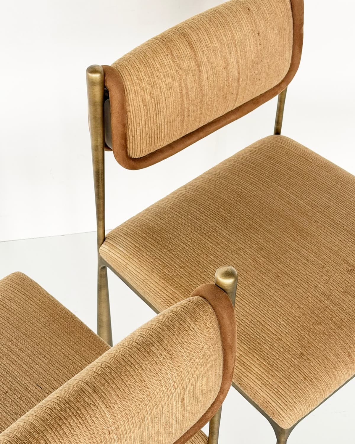 ELVIA upholstered dining chairs with textured tan fabric seats and curved backrests, supported by slim metallic frames.