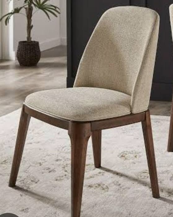 MARA premium dining chair with a softly curved high upholstered back, cream seat and warm walnut wooden frame in an elegant interior.