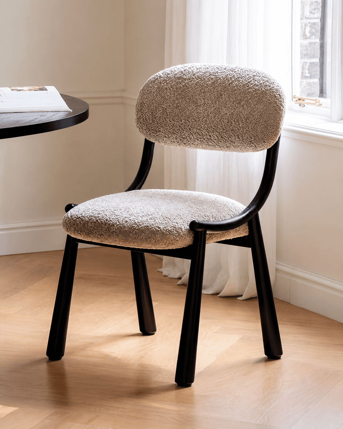 ÉLIA premium upholstered dining chair with rounded cream boucle-style back and seat, curved dark wooden frame and tapered legs.